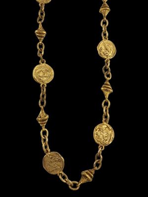 un collier en or composé de pièces suspendues à une chaîne, sur fond noir