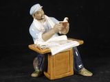 une figurine représentant un homme assis à un bureau en train de lire un livre