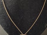 a gold necklace with a pink flower on a black mannequin