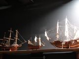 three model ships on a wooden shelf in a dark room