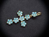 a gold and turquoise cross pendant with pearls on a black background