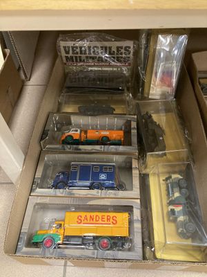 plein de petits camions jouets dans une boîte posée par terre