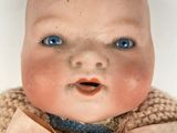 a baby doll with blue eyes wearing a sweater and a bow tie
