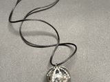 a close up of a necklace with a silver ball on a black cord
