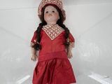 une poupée vêtue d'une robe rouge et d'un chapeau, posée sur un socle