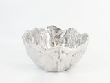 un bol en argent posé sur une surface blanche