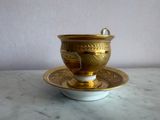 une tasse et une soucoupe dorées posées sur une assiette blanche