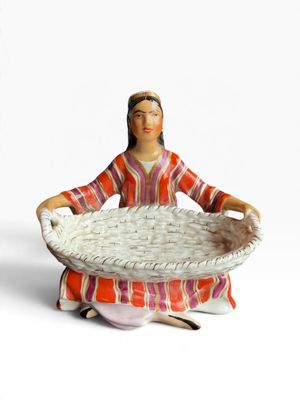 une figurine représentant une femme avec un panier sur les genoux