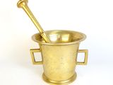 brass mortar and spoon on a white surface with a white background