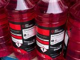 Plusieurs grandes bouteilles contenant un liquide rouge sont posées sur une étagère dans un magasin.