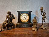 trois figurines en bronze posées sur une table à côté d'une horloge
