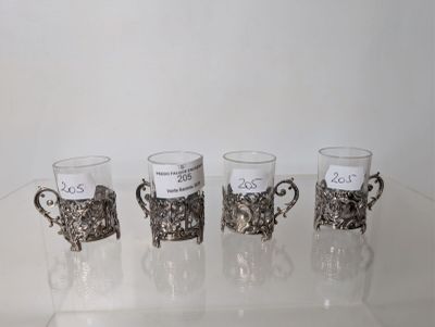 four cups with silver decorations are lined up on a clear table