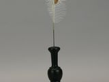 a black vase with a white feather on top of it