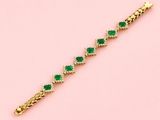 a gold bracelet with emerald stones on a pink background