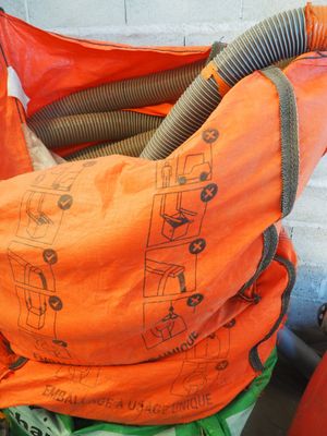 un sac orange auquel est attaché un tuyau, posé au sommet d'un tas d'ordures