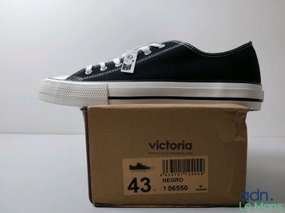 Des Converse noires et blanches sont posées sur une boîte en carton posée sur une surface blanche