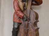 statue représentant un homme jouant du violoncelle et de la contrebasse, posée sur un socle en bois