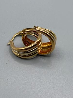 une paire de boucles d'oreilles créoles dorées posées sur un fond gris