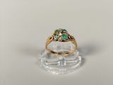 a close up of a gold ring with green stones on a clear surface
