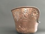 a silver pot with grapes on it sitting on a table