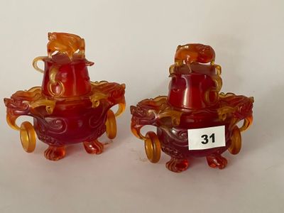 paire de vases en verre rouge munis d'anses, posés sur un fond blanc