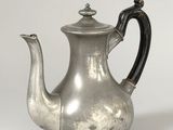 une vieille théière en argent posée sur une table blanche