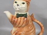 a ceramic cat with a green bow tie and a teapot