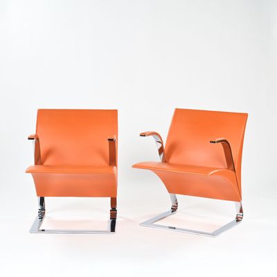 pair of orange leather lounge chairs with chrome legs and arms