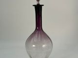 a purple glass bottle with a black top on a white surface
