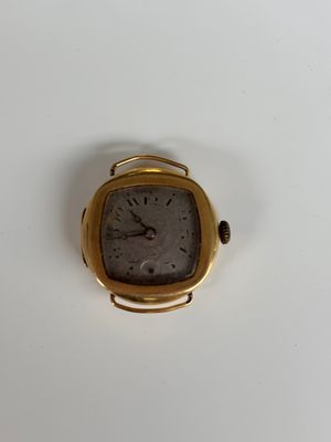 une petite montre en or posée sur une surface blanche