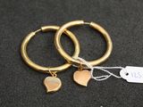 deux boucles d'oreilles en anneau dorées ornées de pendentifs en forme de cœur, sur un fond noir
