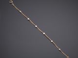 a gold bracelet with pearls and a chain on a gray background