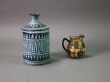 a small vase next to a small jug on a table