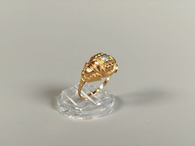 une image représentant une bague en or sertie d'un diamant, posée sur un socle transparent