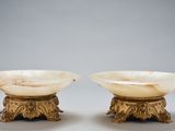 pair of carved marble bowls on pedestals on grey background