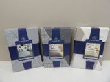 three boxes of bed linens sitting on a table in front of a white wall