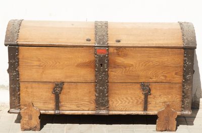 an old wooden chest sitting on top of a sidewalk next to a white wall
