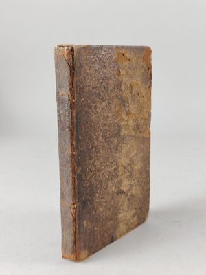 an old book sitting on top of a white table next to a cup