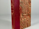 an old book with a red cover sitting on top of a white table