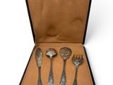four silver spoons in a black case on a white surface