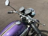 a purple motorcycle parked in a parking lot with a clock on the handlebars
