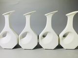 quatre vases blancs sont alignés sur une surface grise