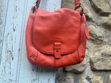 un sac à main en cuir orange accroché au mur, à côté d'un mur en pierre