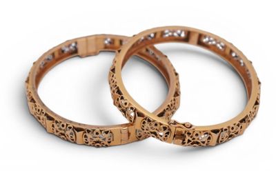 two gold bracelets with diamonds on them on a white surface