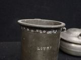 a silver cup with a lid sitting next to a silver pot