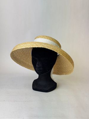 Le chapeau est en paille et est orné d'un ruban blanc autour du bord.