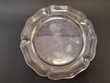une assiette ancienne en argent au bord festonné sur un fond noir