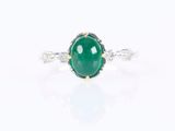 a close up of a green jade and diamond ring on a white surface