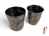 two silver cups sitting next to each other on a white surface