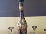 a black and gold vase sitting on a table next to other silver candles
